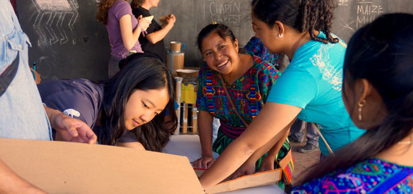 Julia and UVG student Maya work with Maria and Rosa on stage 3 of the workshop. manipulating cardboard cutouts to determine ideal size of cookstove.