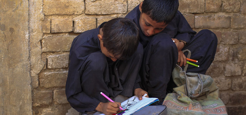 A boy uses colour markers to fill his drawing book outside his makeshift school. REUTERS/Mian Khursheed.