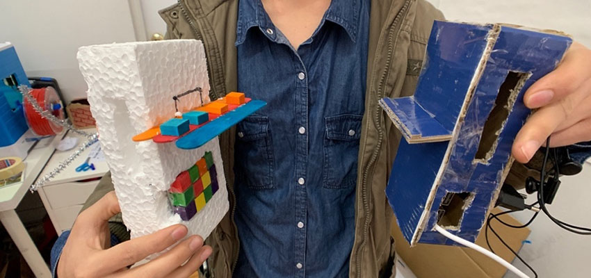 One participant holds up his power bank prototypes to showcase his iteration process for designing during the January 2019 workshop. On the left: a rudimentary sketch model of a phone power bank. On the right: a refined sketch model with accurate dimensions and space to embed electronics.