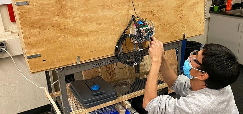 Man crouching to set up an arduino to collect data on the side of a wooden box