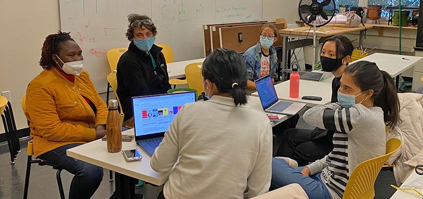 Happy Amos, Dan Sweeney and students sit at a table in D-Lab.