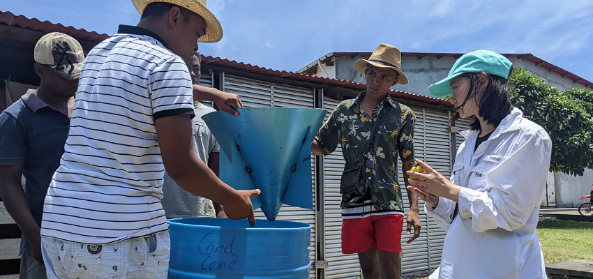 Three people standing around a large blue barrel.