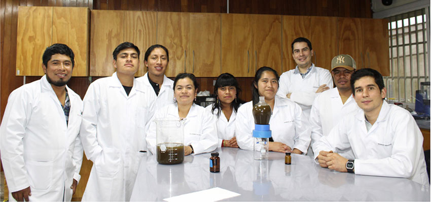 A group of nine men and women in white lab coats behind a research bench looking at the camera.