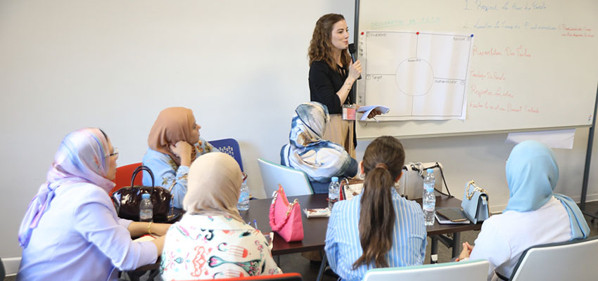 A women standing at a white board in front of a small group of seated people.