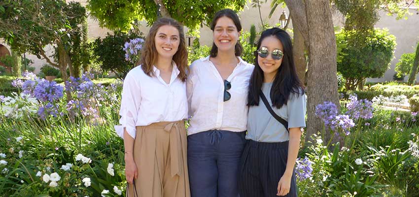 Three smiling women standing close together in front of a lush green background.