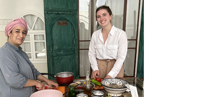 Two smiling women standing over a table of dishes and food.