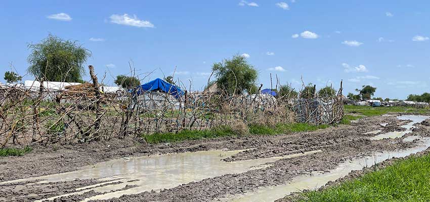 dry muddy road next to fence and rudimentary housing