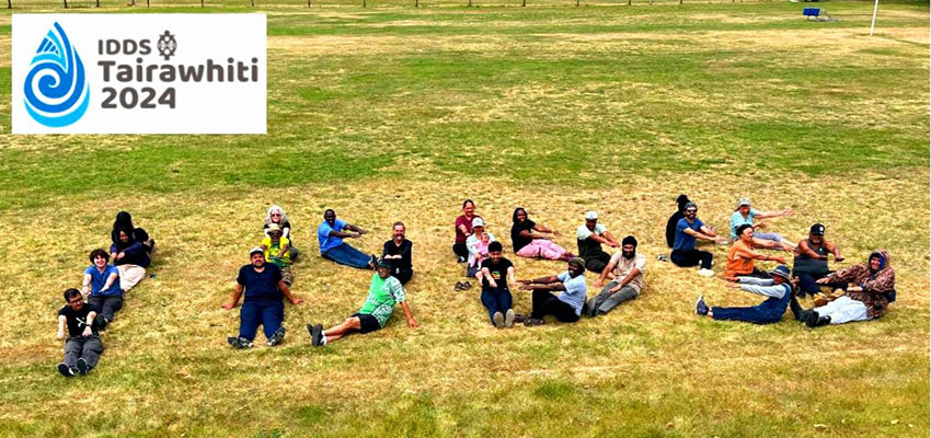 A group of 20+ people lying in field spelling out the letters IDDS.