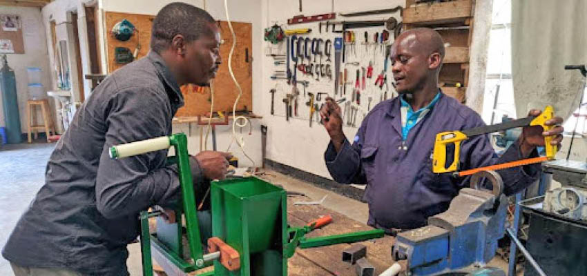 Two men talking over a workshop table.