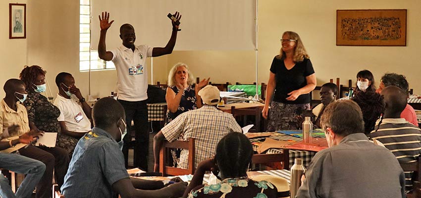 Two people standing presenting to a group seated in front of them.